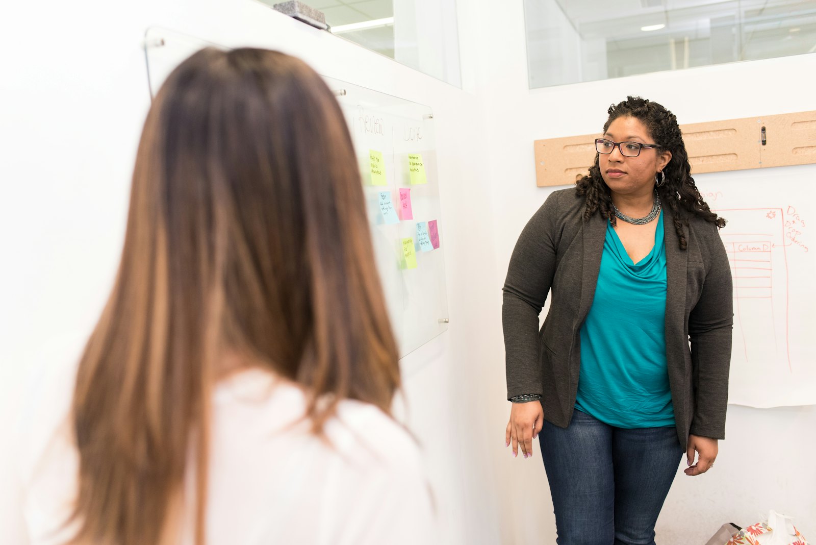 Two colleagues at a whiteboard covered in sticky notes, one explaining while the other listens